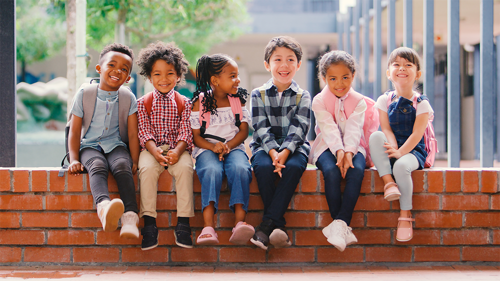 Group of children sitting on a short, brick wall.