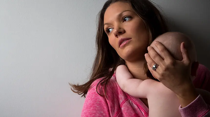 a lady holding a baby, looking away from camera