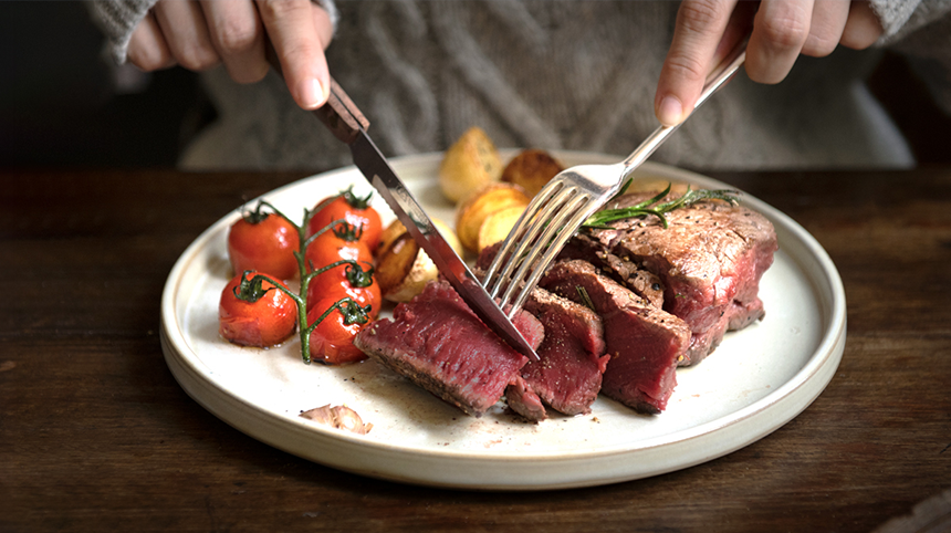 image of hands with knife and fork cutting into steak
