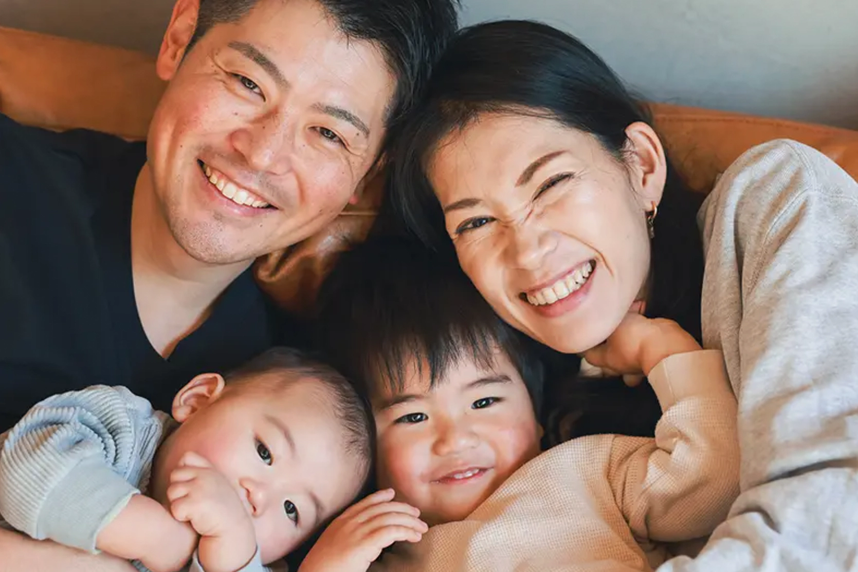 Family of four embracing eachother on a couch while looking at the camera